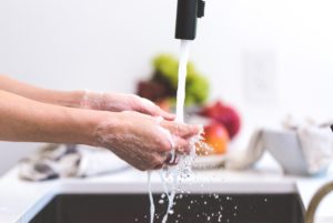 handen wassen onder stromend water met fruit op de achtergrond naast de wastafel